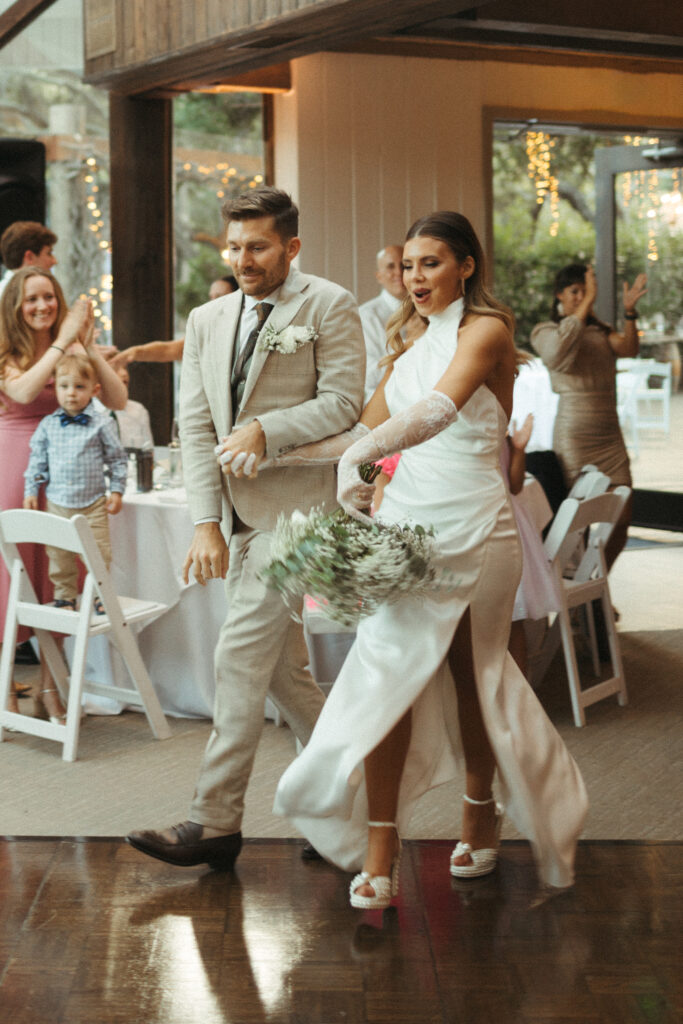bride in satin halter style wedding dress with gloves and groom in khaki plaid suit grand entrance for wedding reception at Calamigos Ranch