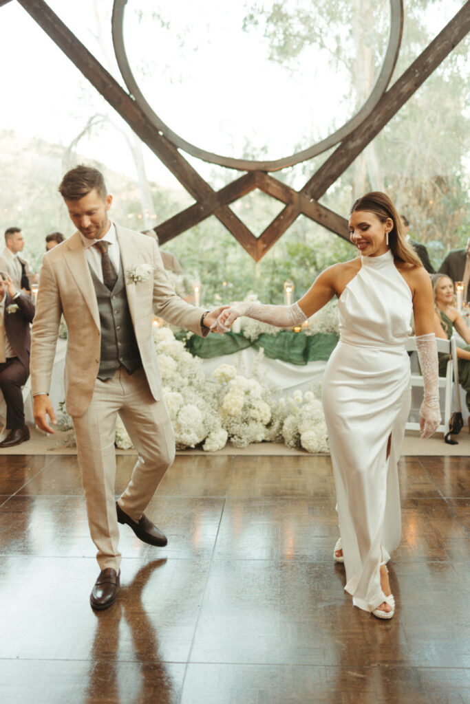 bride in satin halter style wedding dress with gloves and groom in khaki plaid suit first dance at wedding reception at Calamigos Ranch