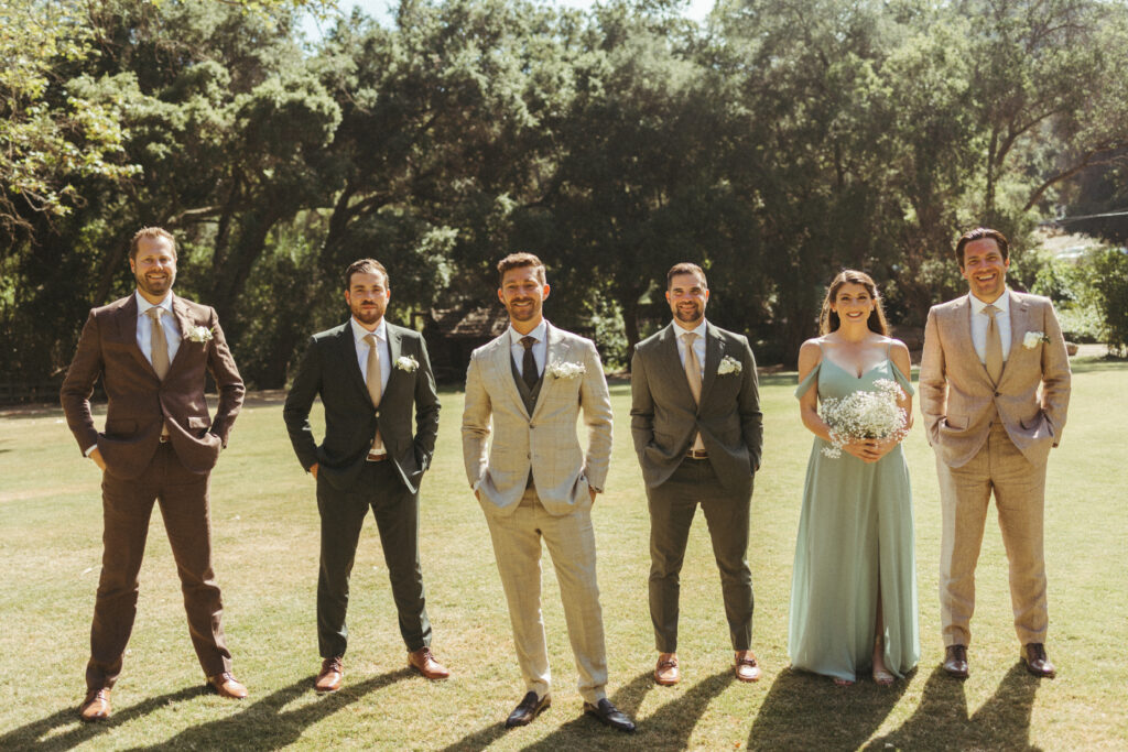 groom in khaki plaid suit stands with wedding party in mix matched outfits