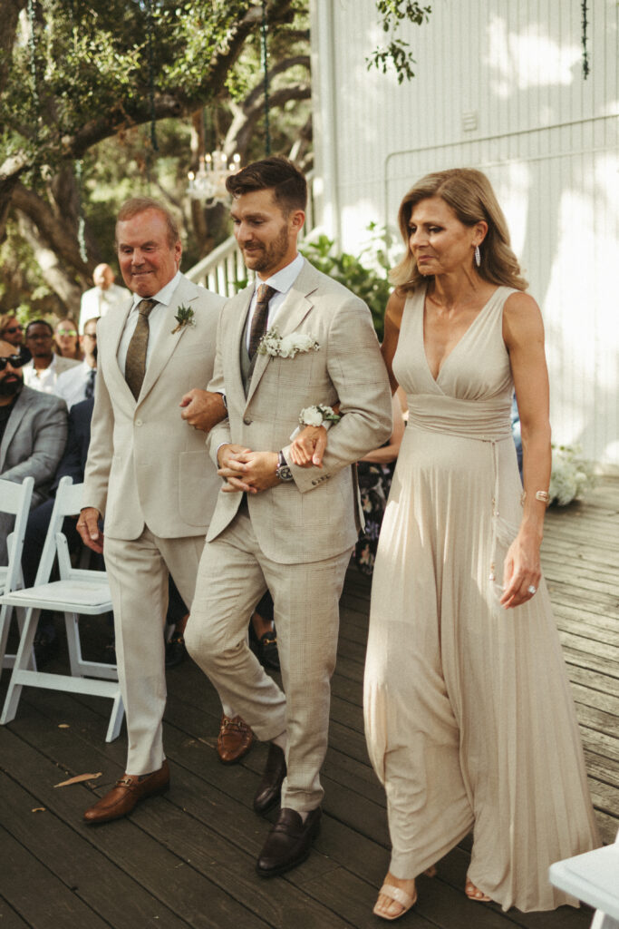 groom in khaki plaid suit walks with parents down aisle