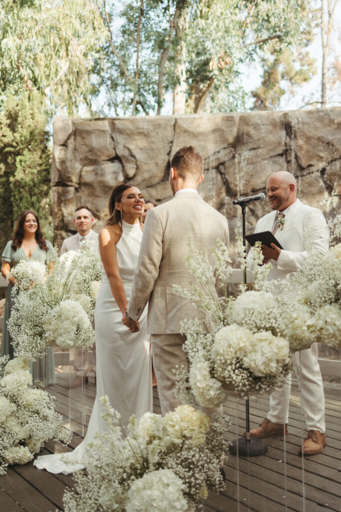 minimalist refined wedding ceremony with waterfall backdrop and acrylic tiered floral arrangements with baby's breath and white flowers 