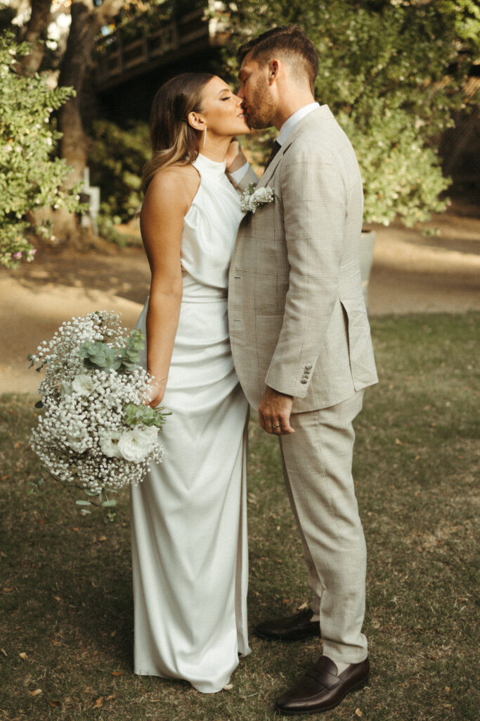 bride in satin halter style wedding dress and groom in khaki plaid suit kissing portrait photos at Calamigos Ranch