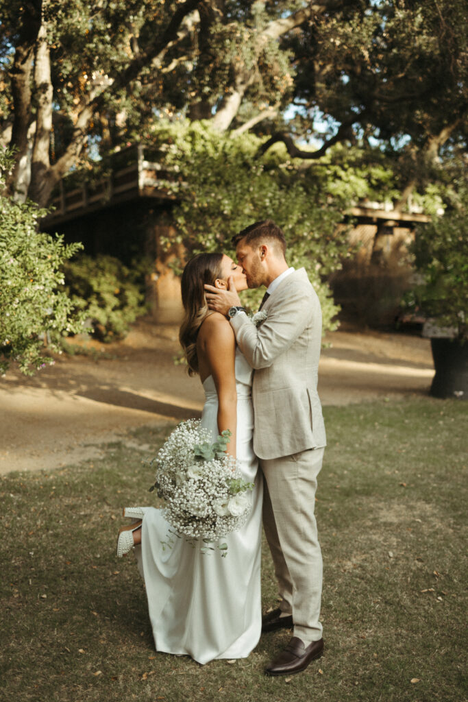 bride in satin halter style wedding dress and groom in khaki plaid suit kissing portrait photos at Calamigos Ranch