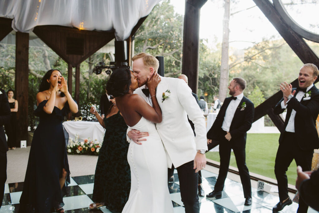 bride in strapless wedding dress kissing groom in white suit during grand entrance at Calamigos Ranch in Los Angeles 