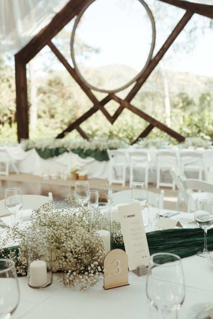 minimalist yet refined wedding reception at Calamigos Ranch with green gauze table runner, candles and baby's breath floral arrangements