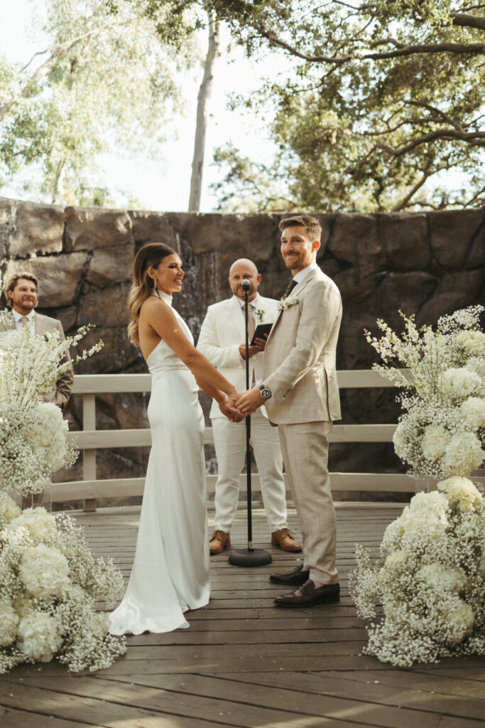 minimalist refined wedding ceremony with waterfall backdrop and acrylic tiered floral arrangements with baby's breath and white flowers 