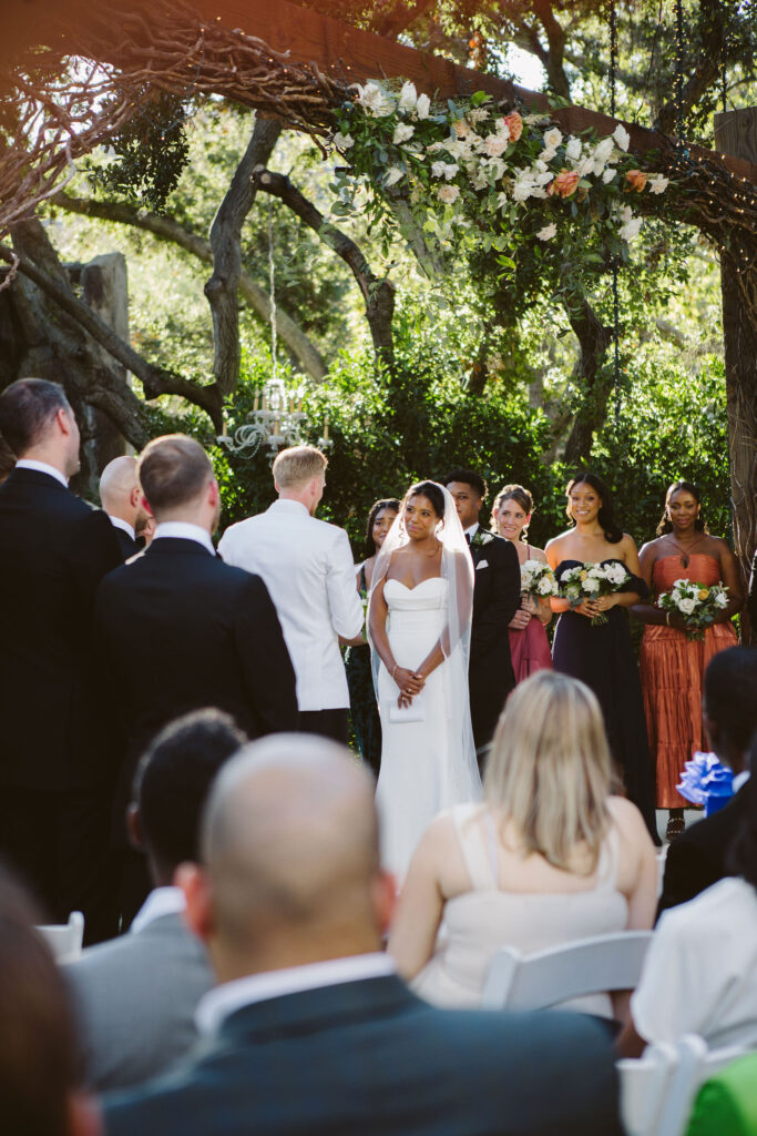 groom in white tuxedo jacket says vows to bride in modern minimalist wedding dress during stylish and timeless wedding ceremony at Calamigos Ranch 