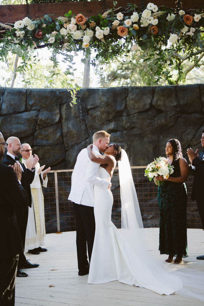 bride and groom kiss in front of waterfall during wedding ceremony at  Calamigos Ranch
