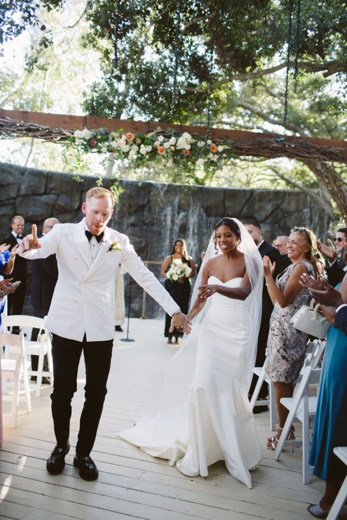 Bride in modern minimalist wedding dress and groom in white tuxedo jacket recessional after wedding ceremony at Calamigos Ranch 