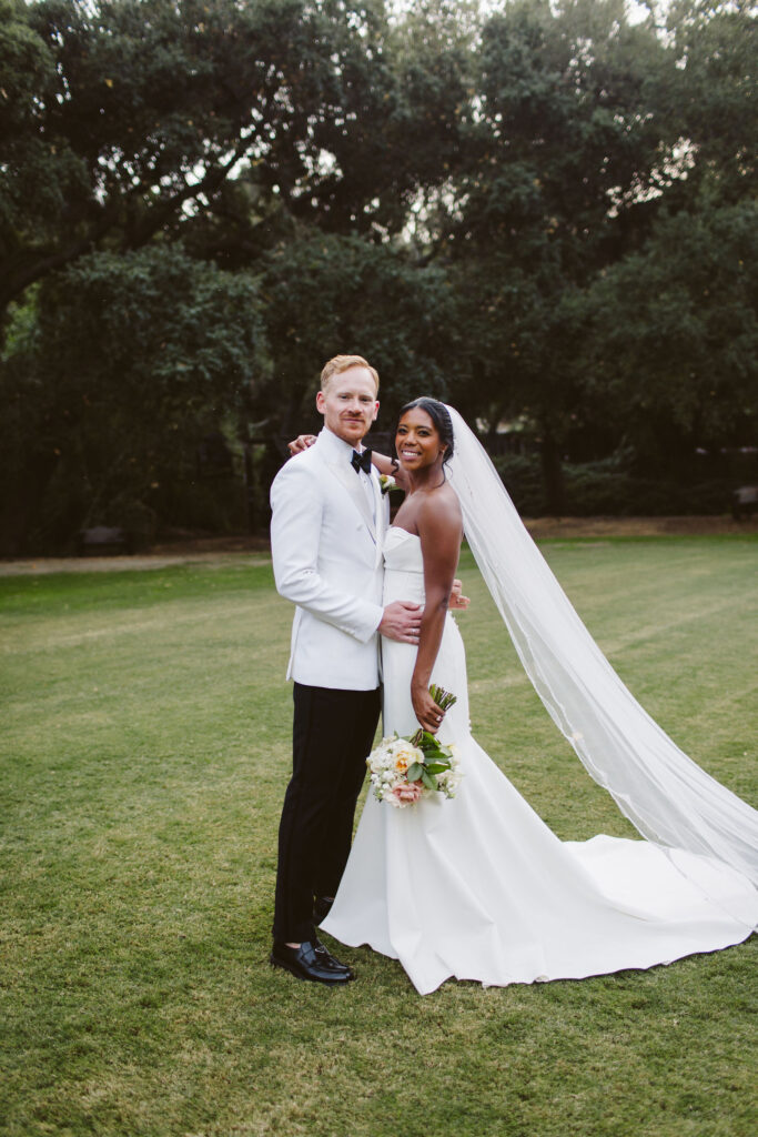 Stylish bride in modern minimalist wedding dress and cathedral veil with groom in white tuxedo jacket at Calamigos Ranch 