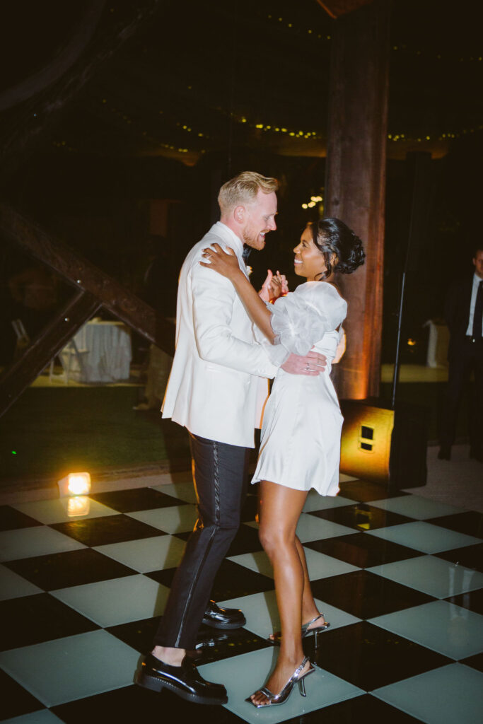 First dance with stylish bride in white mini dress with puff sleeves and square toe silver sling back heels and groom in white tuxedo jacket 
