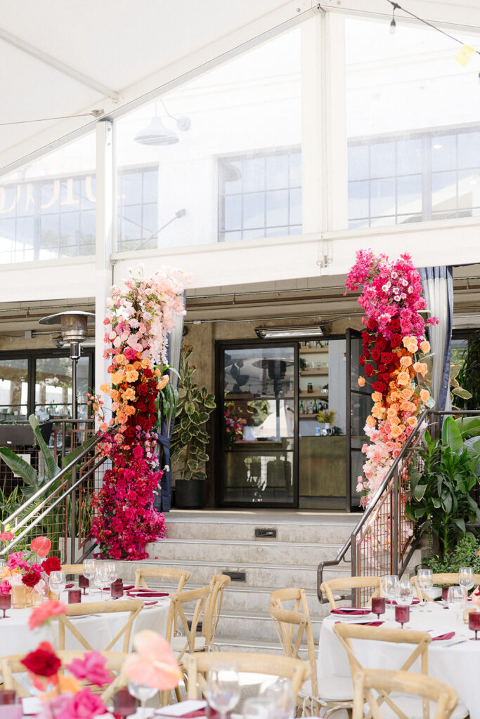 columns wrapped in pink and orange florals frame the stairs leading to a wedding reception dinner in Los Angeles | Feathered Arrow Studio, Los Angeles wedding planner